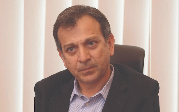 Amir Wain seated in an office, wearing a suit jacket and shirt, focused during an executive meeting.