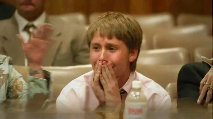 Young Charlie Schockner reacts emotionally in court, wearing a pink shirt and tie, hands over mouth