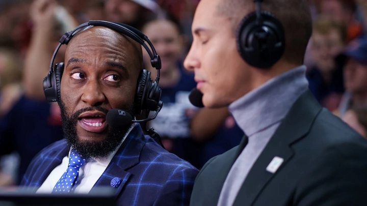 Daymeon Fishback broadcasting live as sports analyst, wearing headset and blue suit at commentary desk