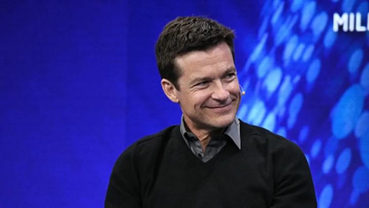 Jason Bateman smiling on stage in black sweater during public talk, featured in net worth biography.