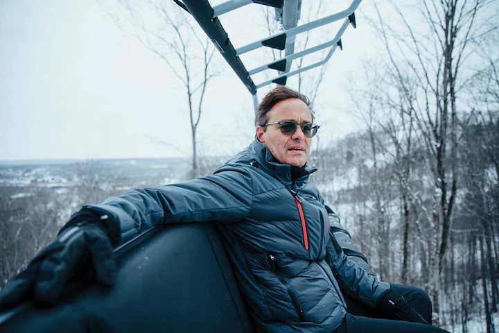John Kircher riding ski lift in winter jacket, featured in John Kircher’s Net Worth 2025 article.