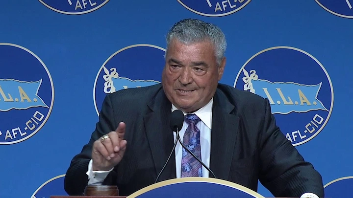Business leader in a suit speaking at a podium with ILA AFL-CIO logos in the background