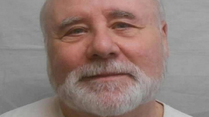 Close-up mugshot of John Edward Robinson with white beard, neutral expression, wearing a light shirt.
