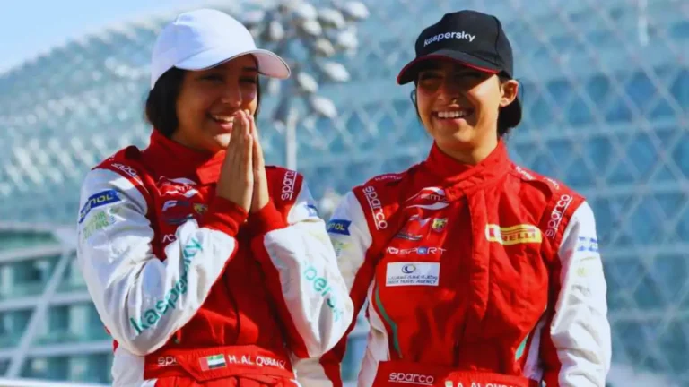 Amna and Hamda Al Qubaisi in red racing suits smiling during a motorsport event.