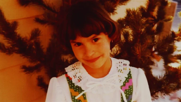Childhood photo of Jonelle Matthews smiling outdoors in a white blouse with green and pink trim.