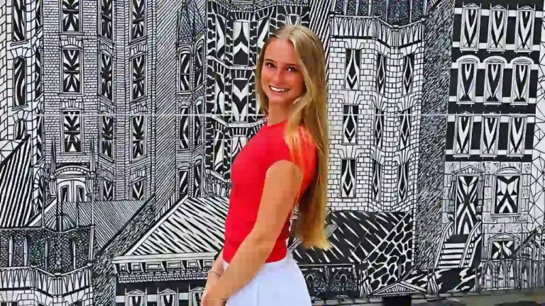 Anna Phelan smiling in a red top and white skirt standing in front of a black-and-white mural.