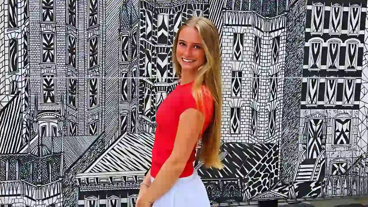 Anna Phelan smiling in a red top and white skirt standing in front of a black-and-white mural.