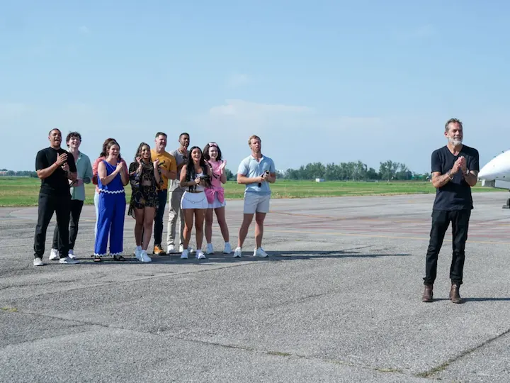 Cast members of Destination X stand on a runway applauding while host Jeffrey Dean Morgan addresses them.