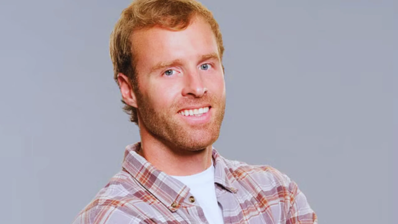Smiling portrait of Biggy Bailey in a plaid shirt on a gray background.