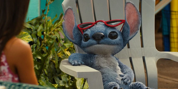 Live-action Stitch wearing red sunglasses, lounging in a chair during a relaxed moment in the Lilo & Stitch remake.