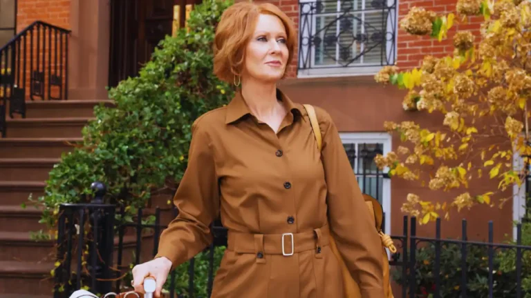 Cynthia Nixon wearing a brown belted jumpsuit walking in a New York neighborhood on the set of And Just Like That.