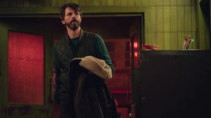 Carl Morck stands in green investigation room holding coat in Netflix’s Dept. Q series scene.