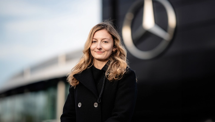 Doriane Pin smiles in a black coat standing in front of a Mercedes-Benz, 2025.