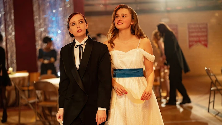 Two teen girls at prom in tuxedo and gown look upward in hopeful wonder.