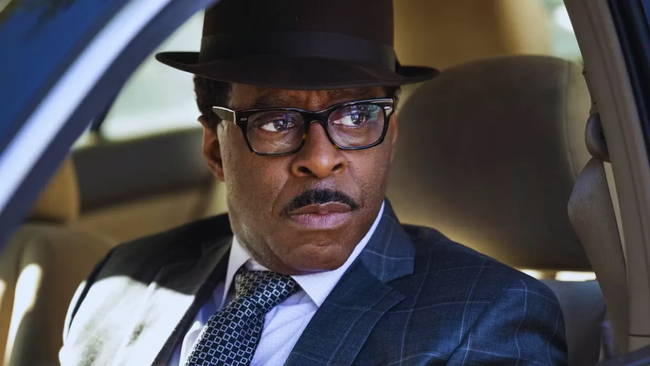 Close-up of a serious man in a fedora and glasses, portraying Cobra Bubbles in the Lilo & Stitch live-action remake.