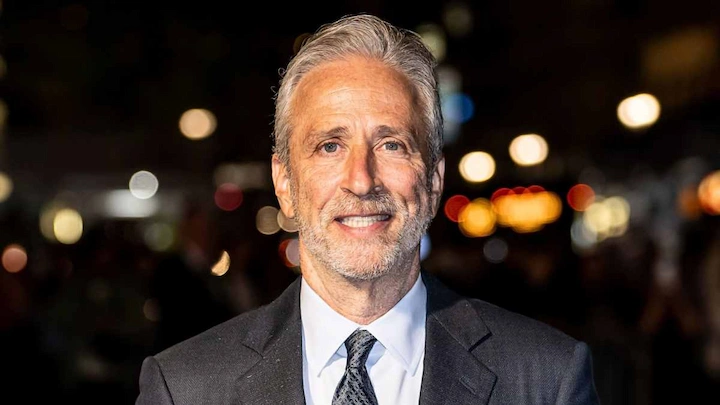 John Stewart smiling in suit at public event, featured in 2025 net worth biography and career success article