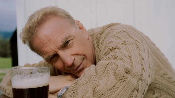 Kevin Costner resting on a table in a beige sweater, responding to Horizon 2 allegations.