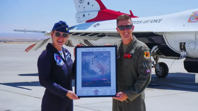 Major Lauren Schlichting and fellow Air Force pilot smile while holding a framed Thunderbird flight photo in front of a jet.