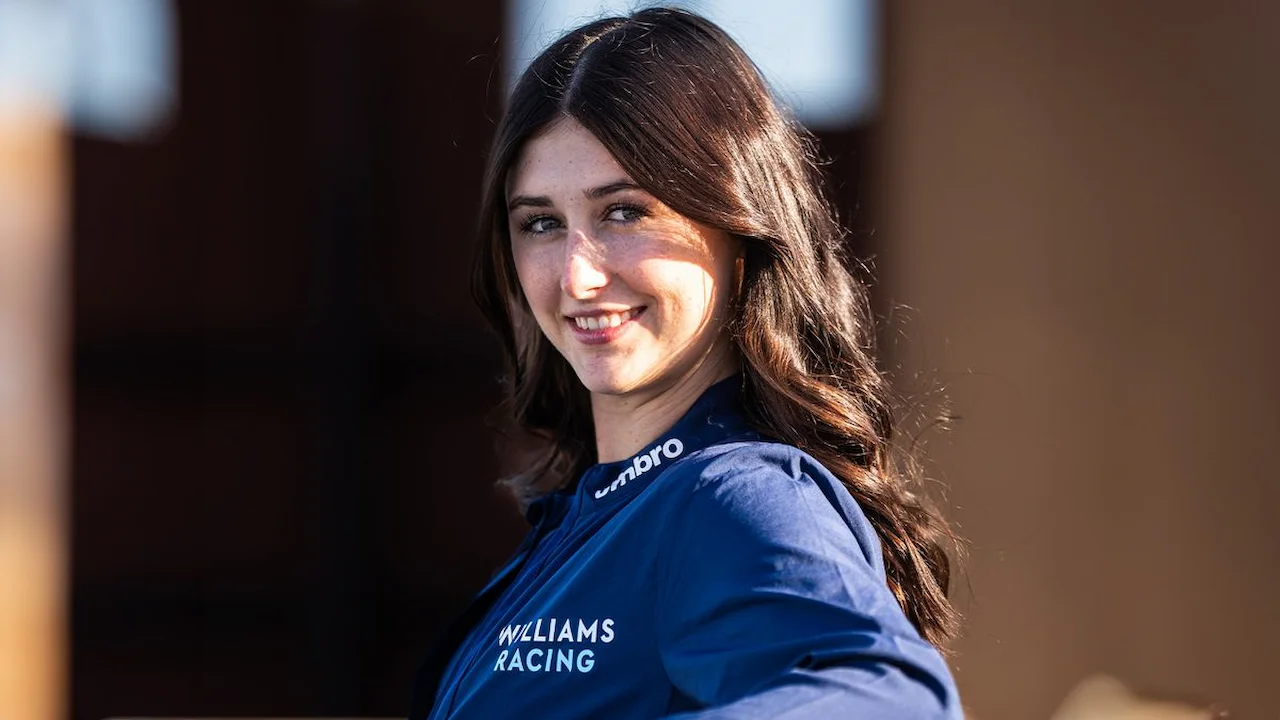 Lia Block smiling in a Williams Racing jacket with wavy brown hair and natural lighting