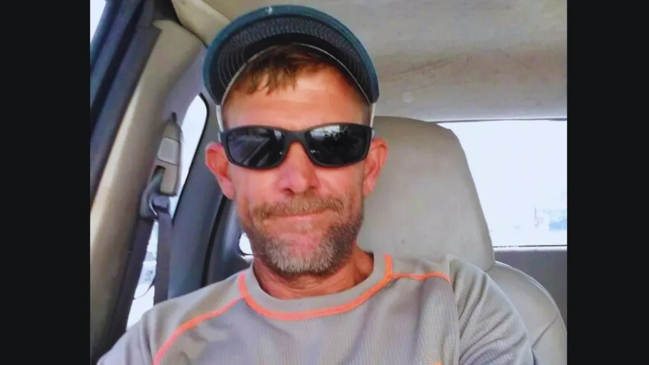 Marc Bruss wearing sunglasses and a cap while sitting inside a vehicle.