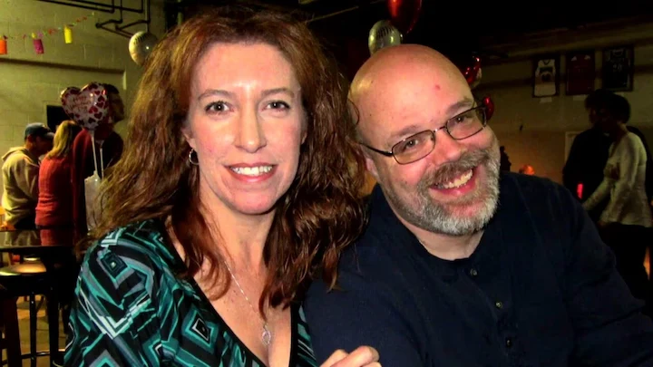 Michelle Mockbee and her husband Dan smiling at a social event with heart-shaped balloons in the background.