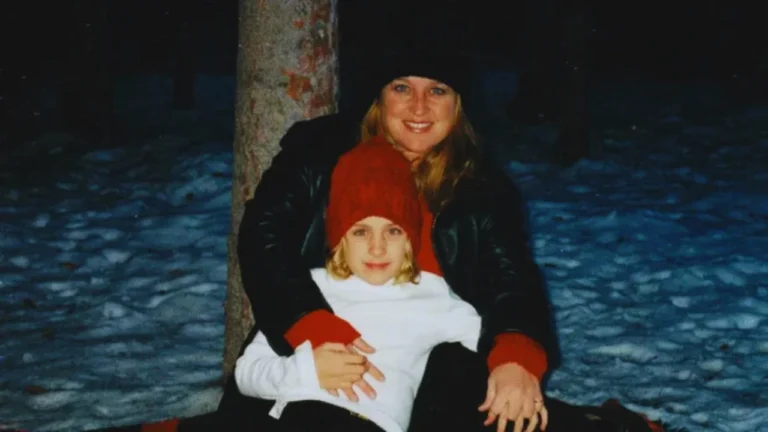Michelle Renee hugging her young daughter Breea in a snowy forest during winter, both wearing red and black winter clothing.