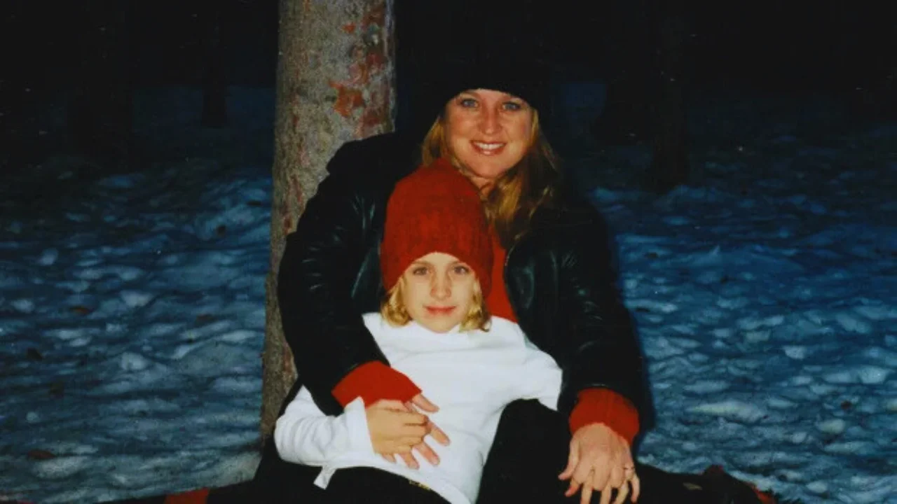 Michelle Renee hugging her young daughter Breea in a snowy forest during winter, both wearing red and black winter clothing.