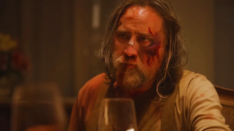Nicolas Cage with a bruised face portraying Robin Feld in Pig, sitting at a table in a tense emotional moment.
