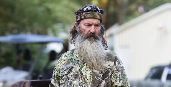 Phil Robertson outdoors wearing camo and a headband, reflecting his Duck Commander roots.