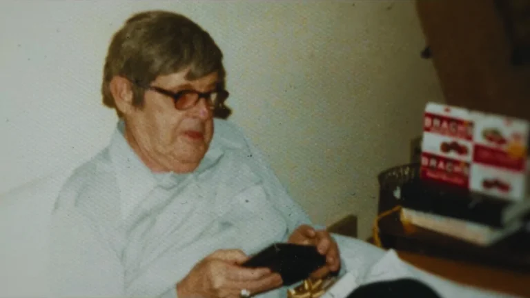 Elderly man sitting indoors holding a wallet, believed to be Raymond West.