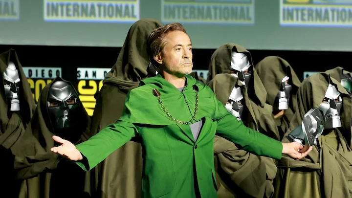 Robert Downey Jr. wearing a green Doctor Doom costume on stage, surrounded by masked figures at San Diego Comic-Con.