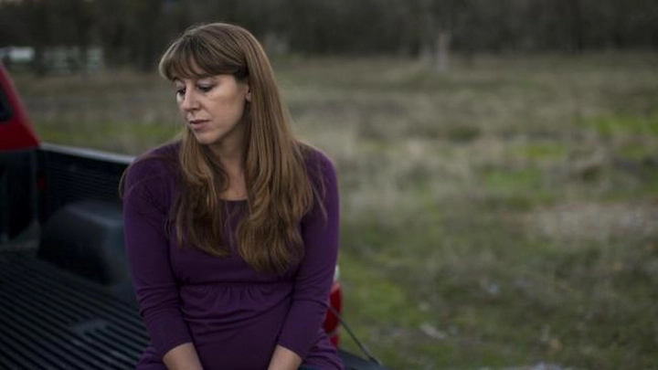Sheila Koester sitting pensively outdoors, wearing a purple dress.