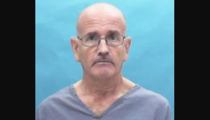 Mugshot of Stanley Jensen in a blue prison uniform against a teal background.