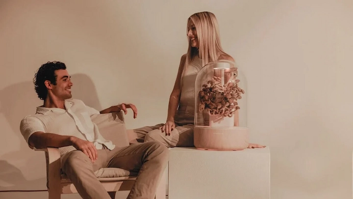 Couple smiling next to Terrashroom mushroom growing device on a white table.