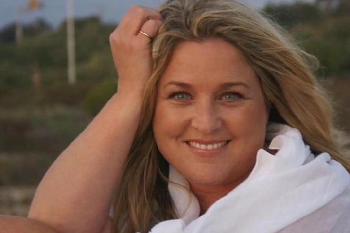 Close-up of Michelle Renee smiling outdoors with windblown blonde hair, wearing a white scarf and light sweater.
