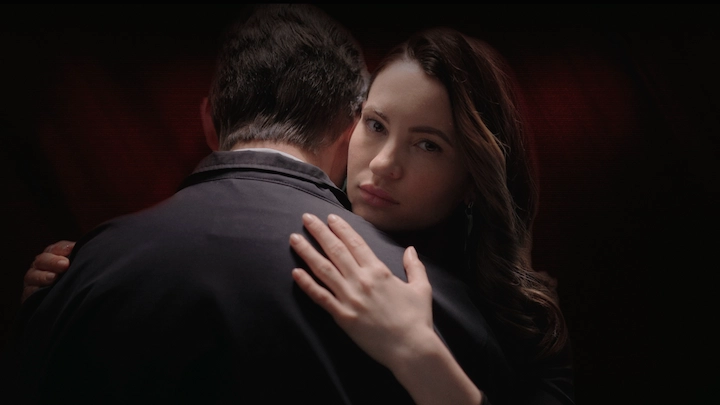 Netflix’s A Widow’s Game lead actress embraces a man while staring with a haunting expression.