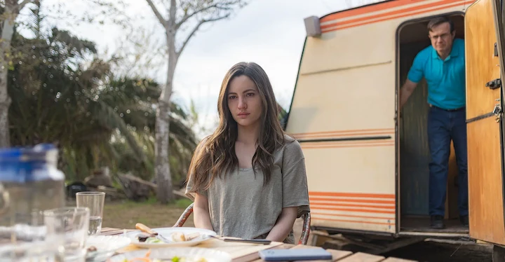 Maje sits outside as Salvo exits a trailer in Netflix’s A Widow’s Game, revealing growing tension.