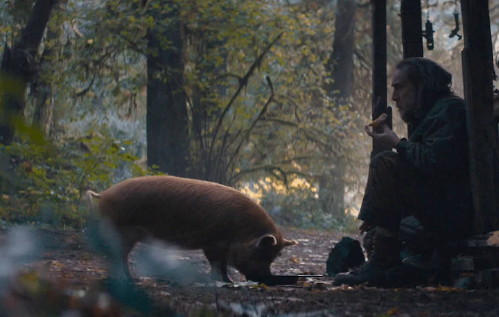 Nicolas Cage as Robin Feld eating quietly beside his truffle pig in the forest from the movie Pig.