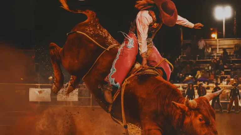 Alexia Huffman bull rider in pink chaps and cowboy hat gripping rope on a bucking bull at rodeo.