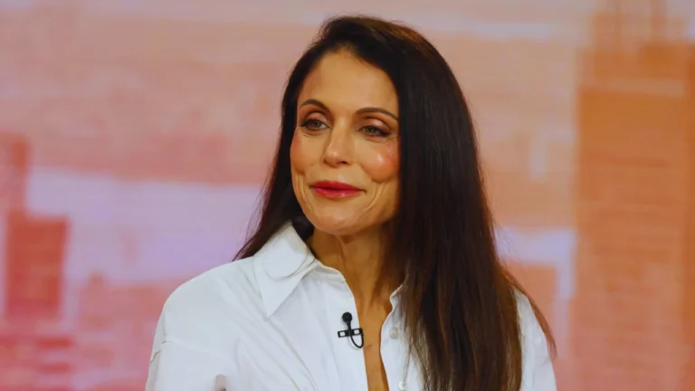 Bethenny Frankel smiles in a white blouse during a television interview, showcasing confidence and grace.