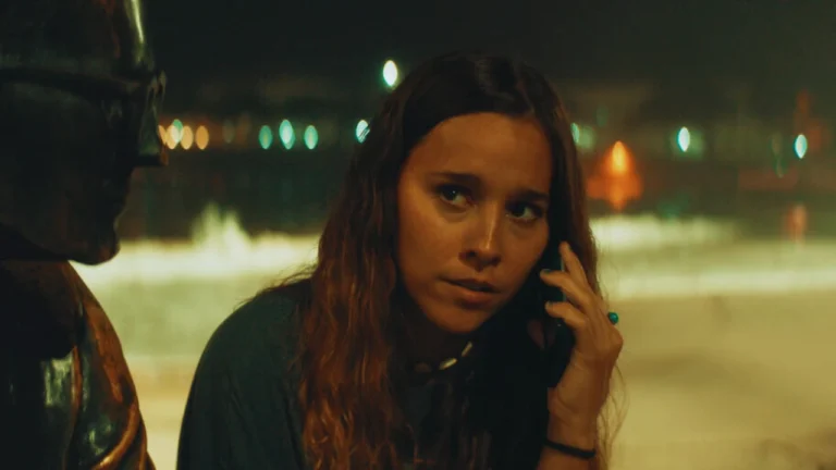 Young woman on phone looks concerned while sitting near statue with blurred lights in background.