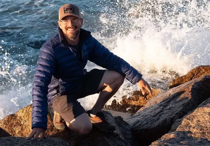 Chris Shontz exploring rocky shore, 2025 net worth journey of adventure, van life, and online success.