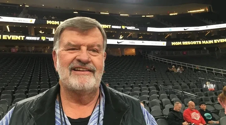 Cliff Findlay smiling at MGM Resorts arena during a sports event, wearing casual vest and shirt.