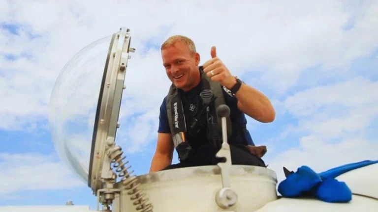 David Lochridge giving thumbs up beside a submersible hatch under a clear blue sky.
