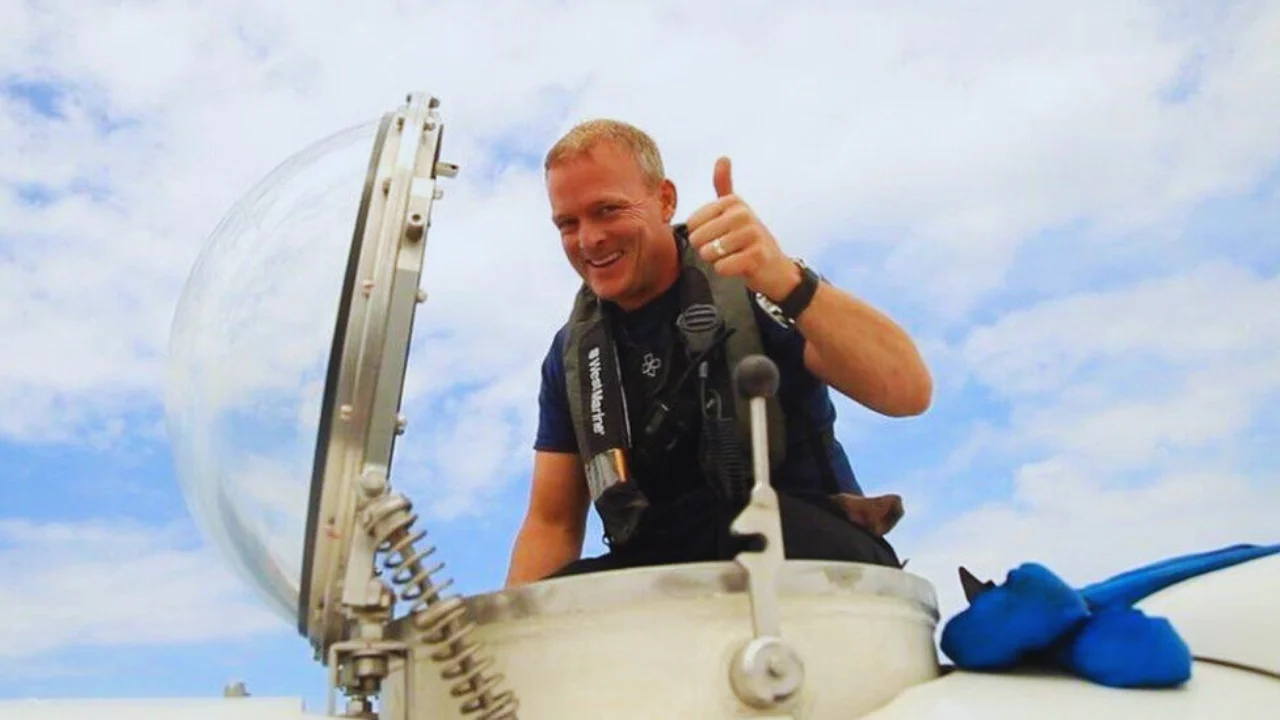 David Lochridge giving thumbs up beside a submersible hatch under a clear blue sky.