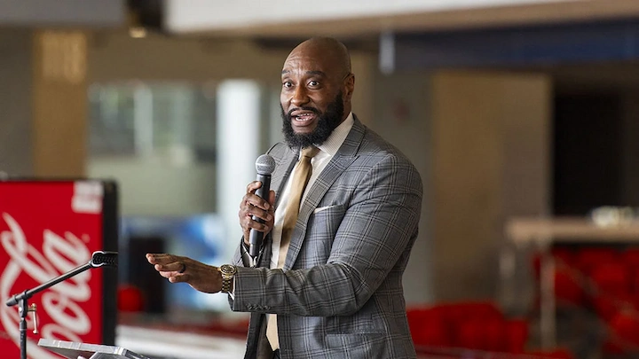 Daymeon Fishback speaking at event in gray suit, holding microphone, sharing insights and experience