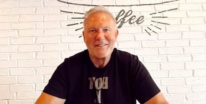 Donnie Wendolyne sitting at a cafe table with a white brick wall and coffee sign in the background.