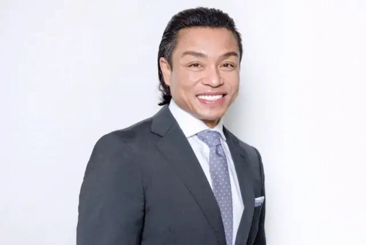 Dr Quang Henderson smiling in a professional suit and tie, posing against a plain white background.