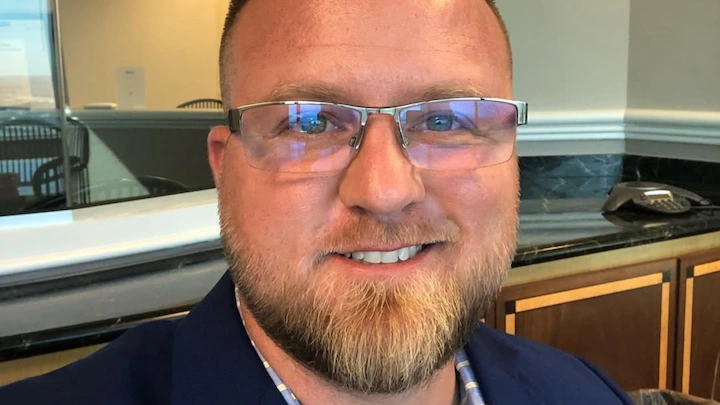 Dustin Bailey smiling in a suit jacket, close-up portrait highlighting his business success in 2025.