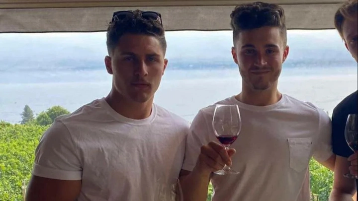 Eric Prockow and friend in white t-shirts holding wine glasses at vineyard with scenic view behind